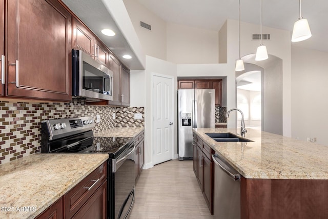 kitchen with pendant lighting, sink, light stone countertops, an island with sink, and stainless steel appliances