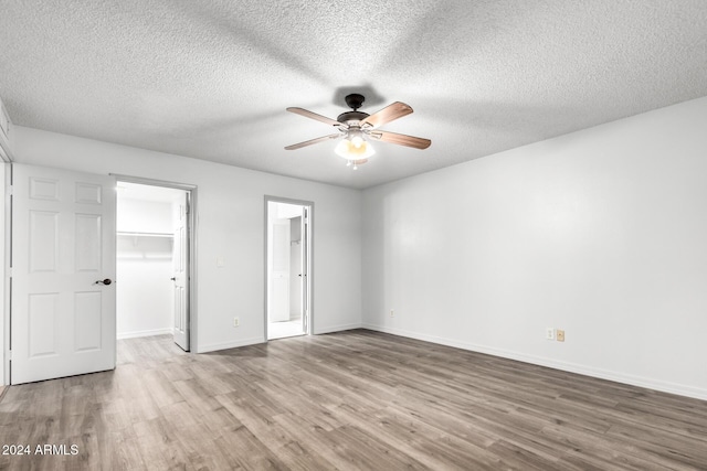 unfurnished bedroom featuring light wood-type flooring, a walk in closet, a textured ceiling, ceiling fan, and a closet