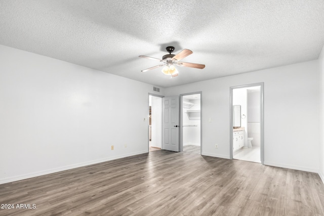 unfurnished bedroom featuring a walk in closet, ensuite bath, hardwood / wood-style flooring, ceiling fan, and a closet