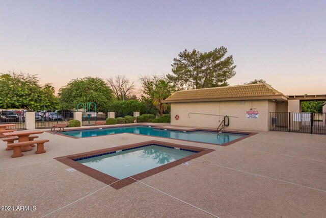 pool at dusk with a hot tub and a patio area