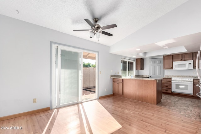 kitchen with kitchen peninsula, a textured ceiling, white appliances, and light hardwood / wood-style floors