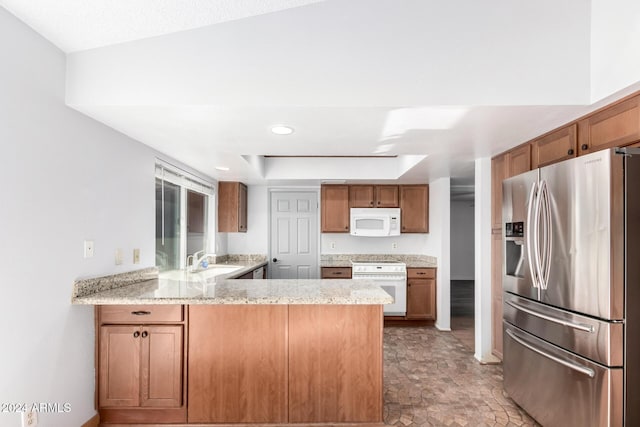 kitchen featuring light stone counters, sink, white appliances, and kitchen peninsula