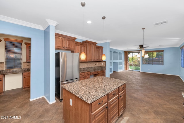 kitchen with pendant lighting, ceiling fan, ornamental molding, a kitchen island, and stainless steel refrigerator