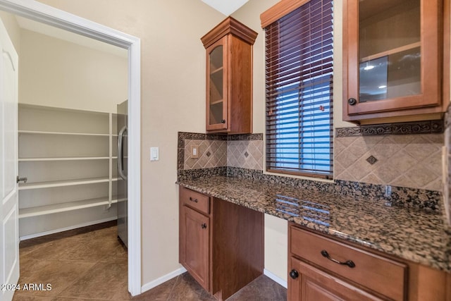 kitchen featuring tasteful backsplash, dark stone countertops, dark tile patterned floors, and stainless steel refrigerator