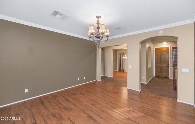 empty room featuring a chandelier, wood-type flooring, and crown molding