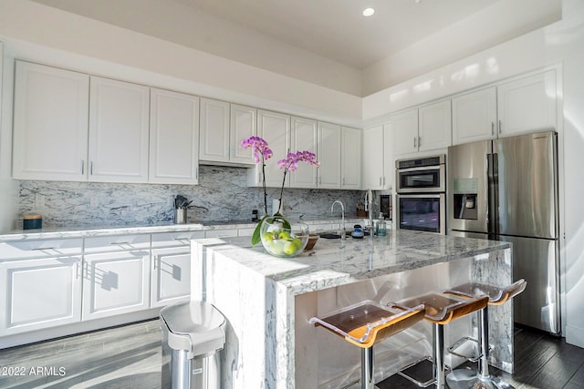 kitchen with white cabinets, light stone countertops, wood finished floors, tasteful backsplash, and appliances with stainless steel finishes