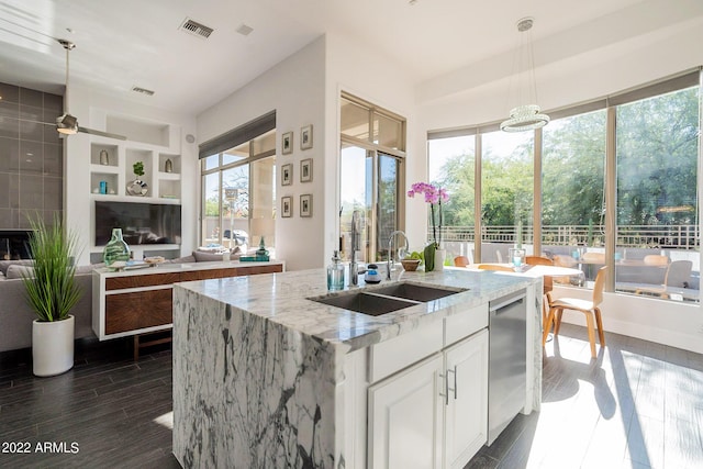 kitchen featuring light stone counters, a sink, hanging light fixtures, visible vents, and dark wood-type flooring