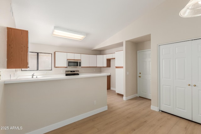 15087 N 86th Dr, Peoria, AZ 85381 - kitchen with vaulted ceiling, appliances with stainless steel finishes, a peninsula, white cabinets, and light wood-style floors