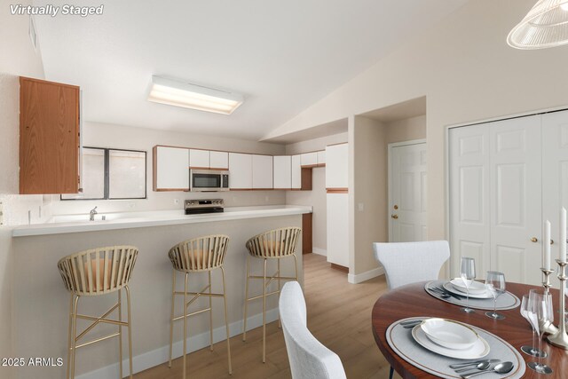 15087 N 86th Dr, Peoria, AZ 85381 - kitchen featuring white cabinetry, lofted ceiling, light wood finished floors, a peninsula, and appliances with stainless steel finishes