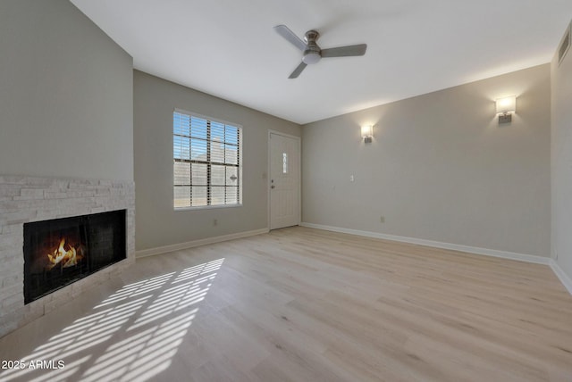 unfurnished living room with ceiling fan, a stone fireplace, and light hardwood / wood-style floors