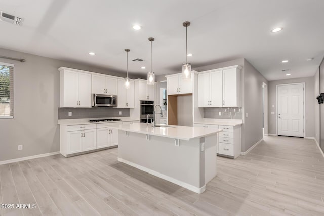 kitchen with white cabinetry, appliances with stainless steel finishes, a center island with sink, and pendant lighting