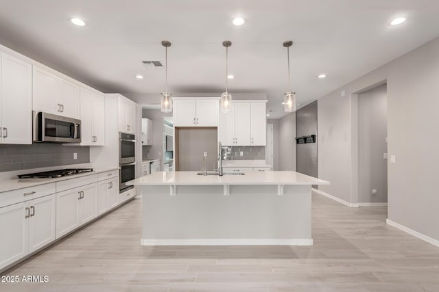 kitchen with a kitchen island with sink, sink, decorative light fixtures, and stainless steel appliances