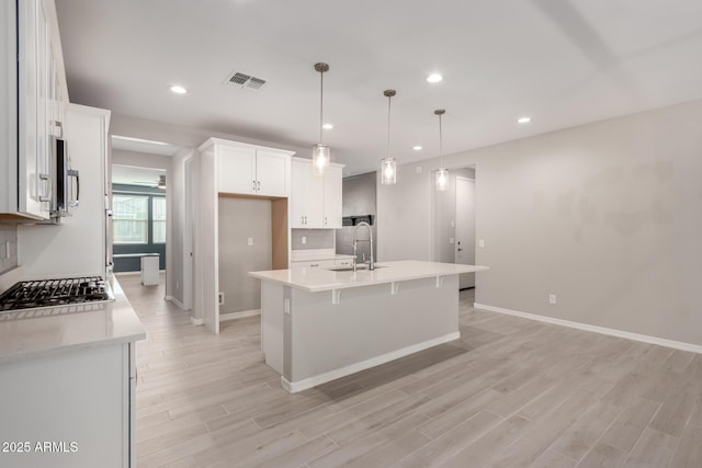 kitchen with sink, light hardwood / wood-style flooring, a kitchen island with sink, white cabinets, and decorative light fixtures