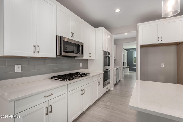 kitchen featuring stainless steel appliances, light stone countertops, white cabinets, and decorative light fixtures