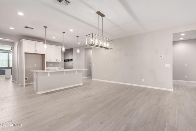 kitchen featuring hanging light fixtures, white cabinetry, a kitchen island with sink, and light hardwood / wood-style flooring