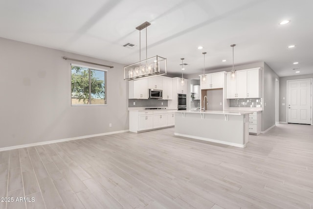 kitchen featuring appliances with stainless steel finishes, a kitchen island with sink, hanging light fixtures, and white cabinets