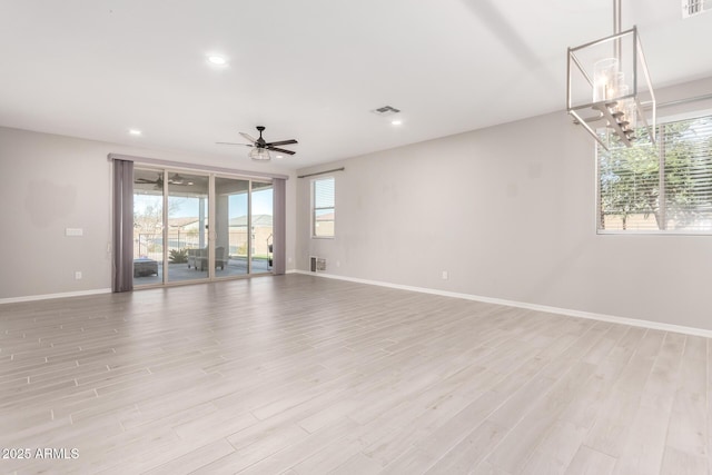 empty room featuring a healthy amount of sunlight, ceiling fan with notable chandelier, and light hardwood / wood-style flooring