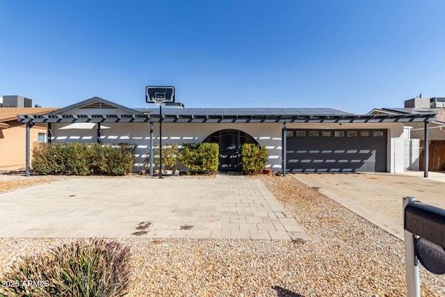 view of front of home with driveway, stucco siding, an attached garage, and roof mounted solar panels