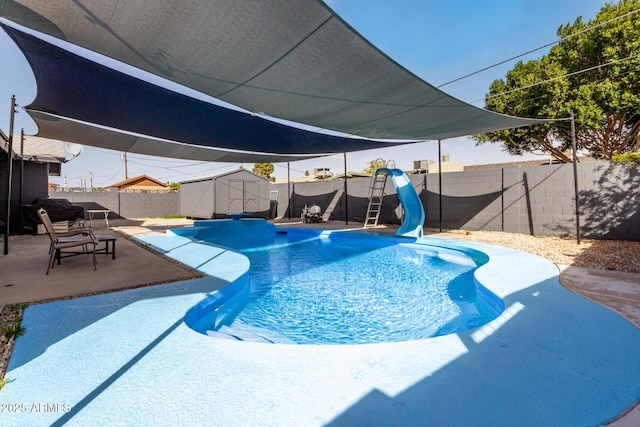 view of swimming pool with a storage shed, a patio, a fenced backyard, a water slide, and an outdoor structure