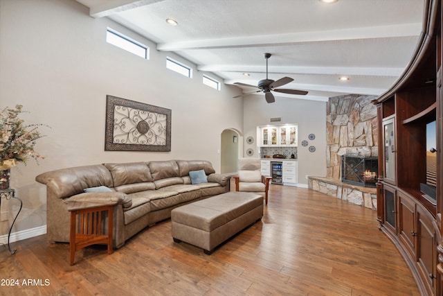 living room with vaulted ceiling with beams, a stone fireplace, wood-type flooring, and ceiling fan