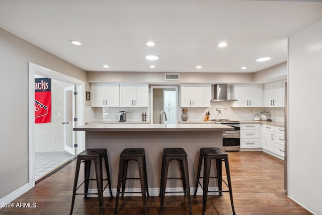 kitchen with wall chimney exhaust hood, a kitchen breakfast bar, stainless steel range, and white cabinets