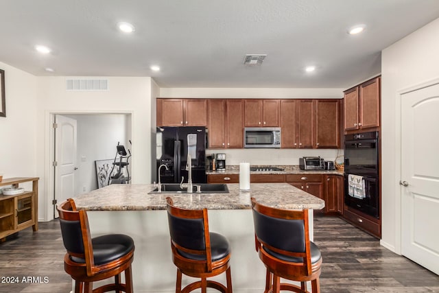 kitchen with black appliances, dark hardwood / wood-style flooring, a center island with sink, and a breakfast bar