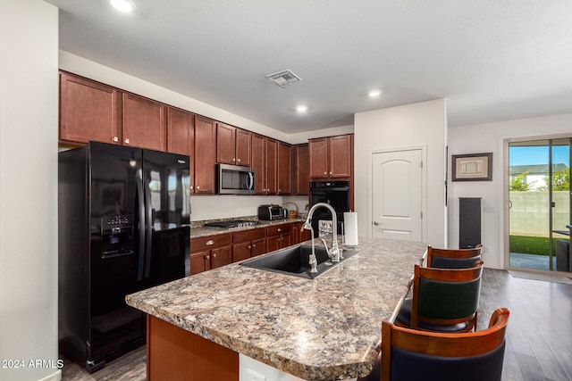 kitchen with black appliances, an island with sink, and hardwood / wood-style floors