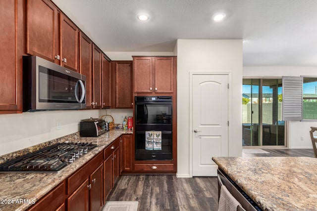 kitchen with gas stovetop, light stone counters, dark hardwood / wood-style flooring, double oven, and a textured ceiling