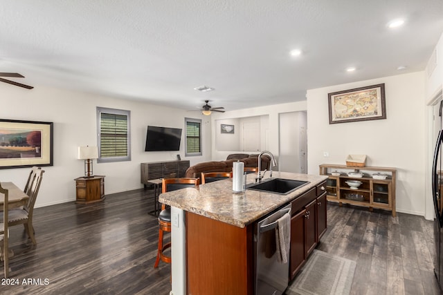 kitchen featuring dishwasher, dark wood-type flooring, a center island with sink, sink, and light stone countertops