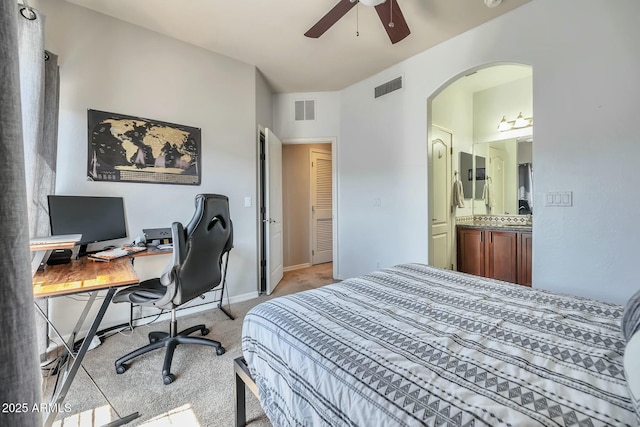 bedroom with ensuite bath, arched walkways, visible vents, and light carpet