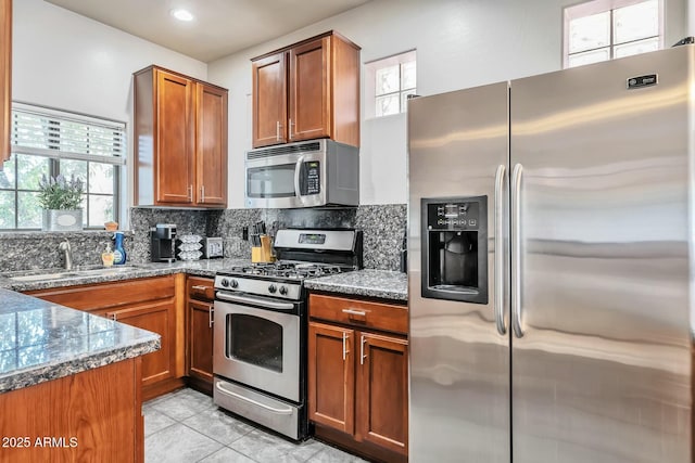 kitchen featuring brown cabinets, a sink, tasteful backsplash, appliances with stainless steel finishes, and light tile patterned flooring