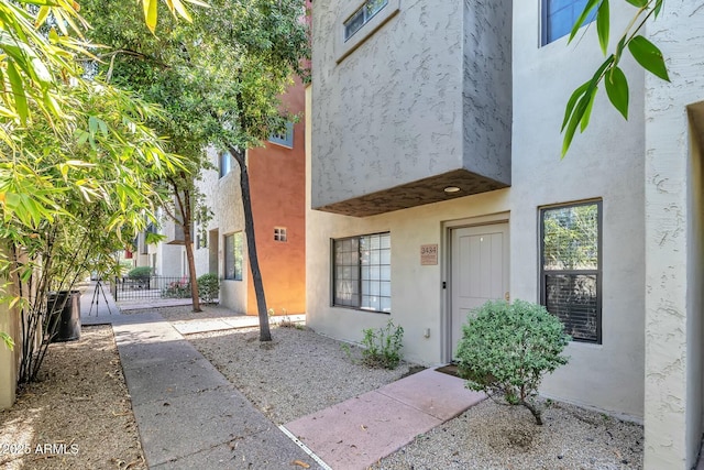 property entrance with a gate, fence, and stucco siding