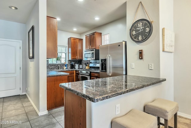 kitchen with tasteful backsplash, a breakfast bar, dark stone countertops, a peninsula, and stainless steel appliances