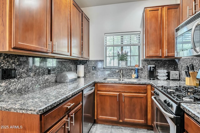 kitchen with dark stone counters, decorative backsplash, brown cabinets, stainless steel appliances, and a sink