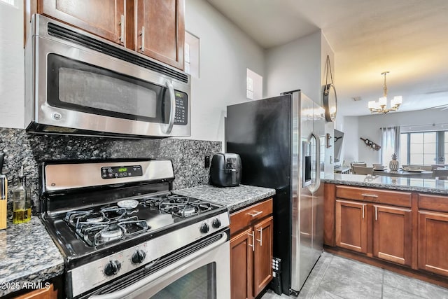 kitchen with stone counters, brown cabinets, stainless steel appliances, tasteful backsplash, and a chandelier