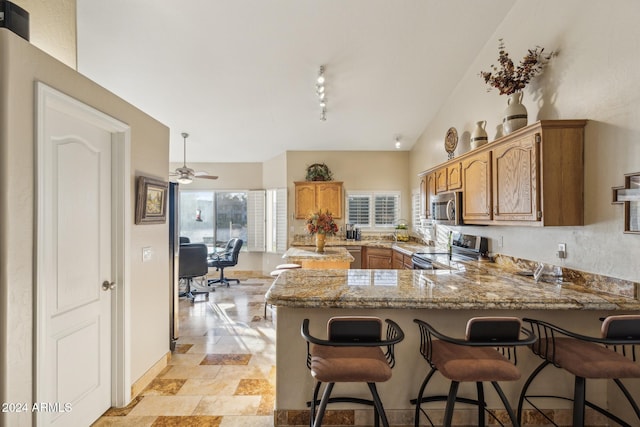 kitchen with lofted ceiling, rail lighting, light stone counters, appliances with stainless steel finishes, and kitchen peninsula