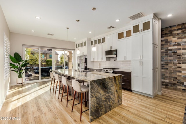 kitchen with sink, stainless steel appliances, light stone counters, an island with sink, and decorative light fixtures