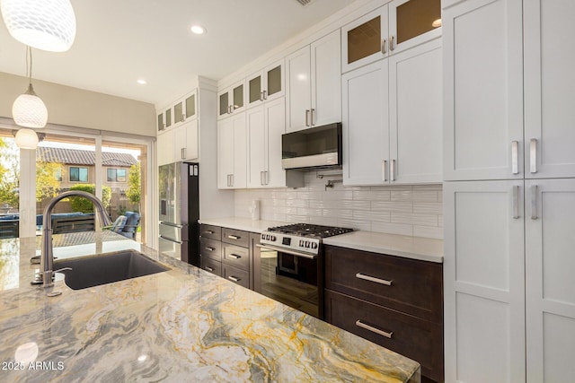 kitchen featuring sink, white cabinets, hanging light fixtures, stainless steel appliances, and light stone countertops