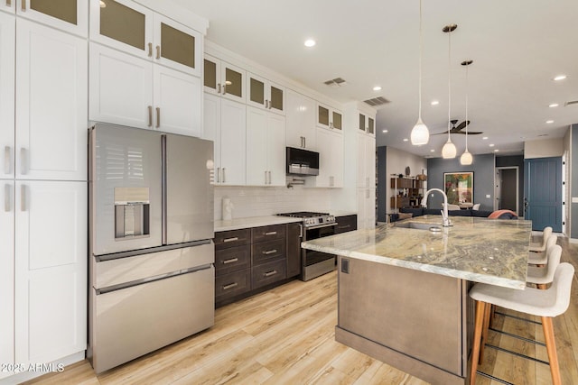 kitchen featuring stainless steel range with gas cooktop, refrigerator with ice dispenser, light stone countertops, a kitchen island with sink, and white cabinets