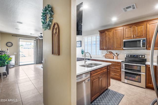 kitchen with a textured ceiling, stainless steel appliances, sink, light tile patterned flooring, and ceiling fan