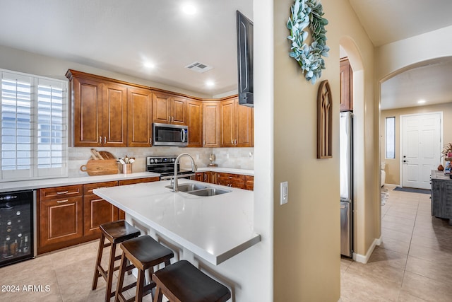 kitchen featuring sink, light tile patterned flooring, appliances with stainless steel finishes, a breakfast bar area, and beverage cooler