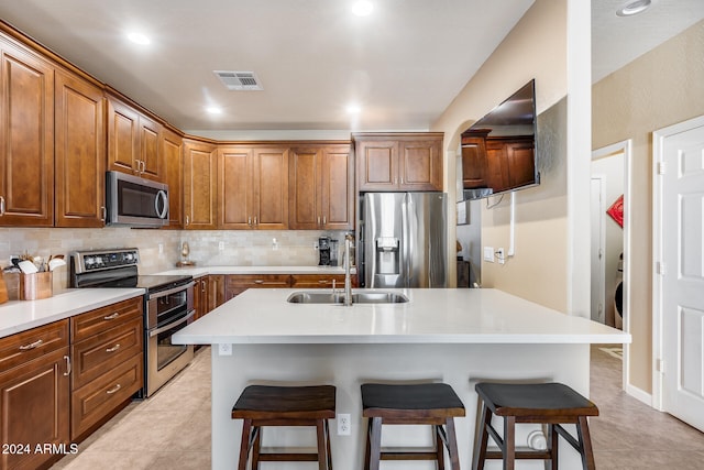 kitchen with appliances with stainless steel finishes, tasteful backsplash, sink, a kitchen island with sink, and a breakfast bar