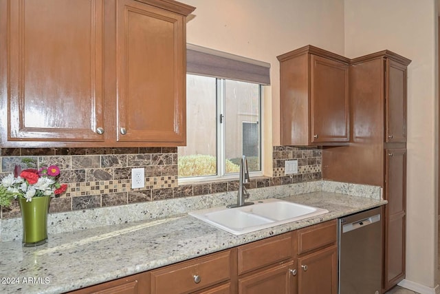 kitchen featuring backsplash, light stone counters, stainless steel dishwasher, and sink