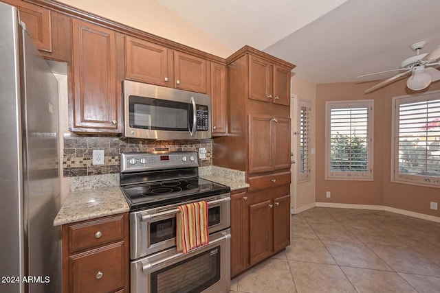 kitchen featuring lofted ceiling, light tile patterned floors, appliances with stainless steel finishes, tasteful backsplash, and light stone counters