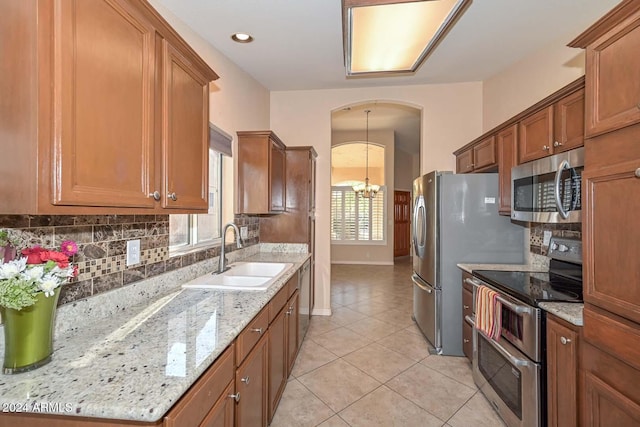 kitchen featuring light stone countertops, appliances with stainless steel finishes, a chandelier, and sink