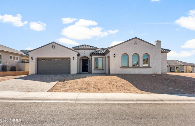 mediterranean / spanish home with decorative driveway, an attached garage, a tile roof, and stucco siding