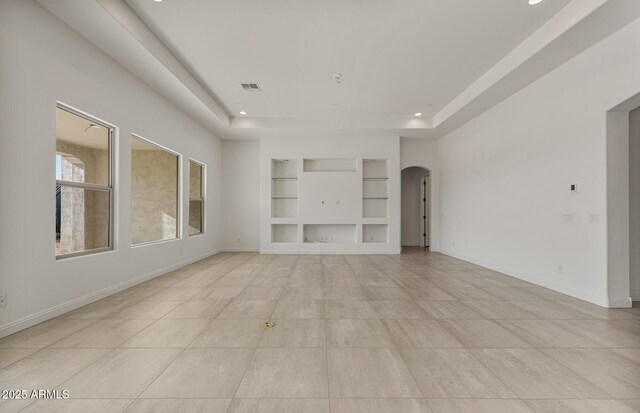 unfurnished living room with built in features, a tray ceiling, arched walkways, recessed lighting, and baseboards