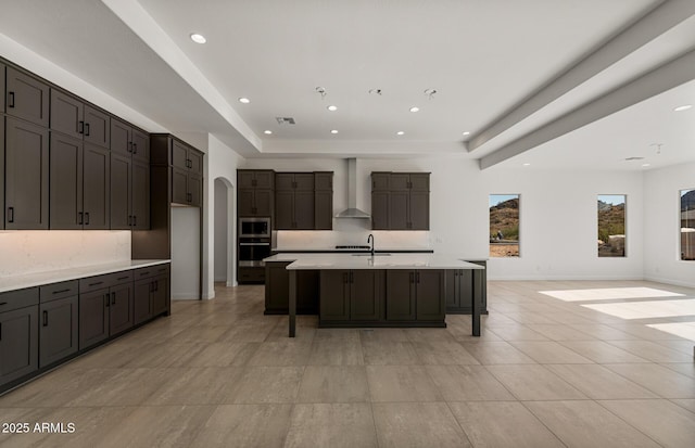 kitchen with appliances with stainless steel finishes, arched walkways, a raised ceiling, and wall chimney exhaust hood