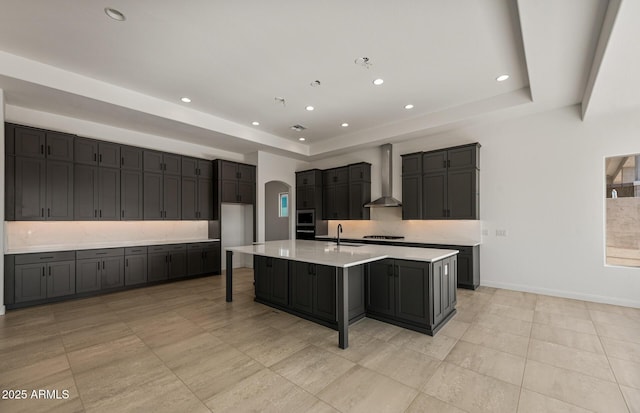 kitchen featuring a tray ceiling, a sink, arched walkways, and wall chimney exhaust hood