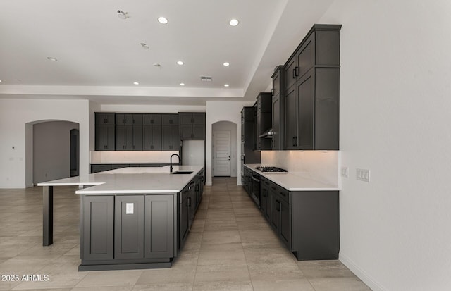 kitchen with arched walkways, a spacious island, recessed lighting, light countertops, and a sink